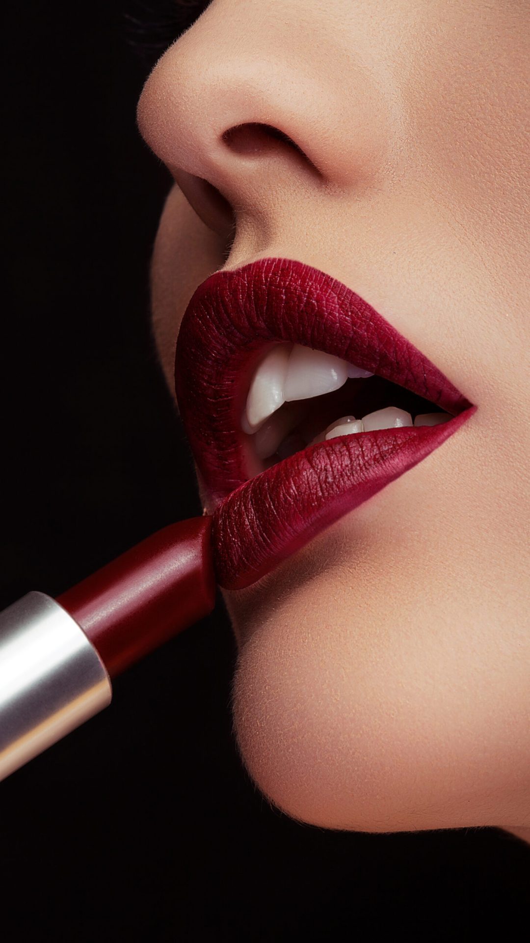 Applying red lipstick on lips in close up photo on black background. Beauty and make up
